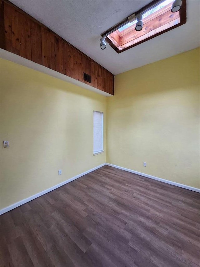 spare room featuring dark hardwood / wood-style flooring, a skylight, and a textured ceiling