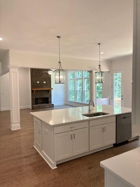 kitchen with a brick fireplace, pendant lighting, dishwasher, white cabinetry, and an island with sink