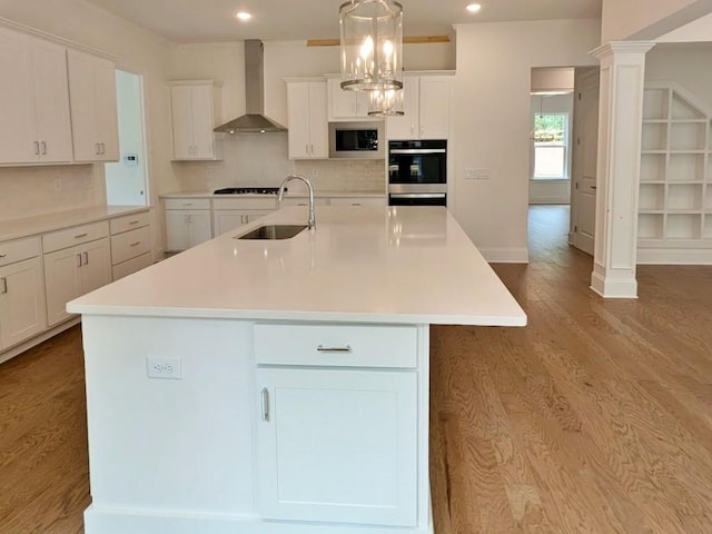 kitchen with pendant lighting, backsplash, a center island with sink, wall chimney range hood, and sink