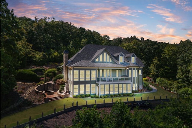 back house at dusk featuring a sunroom and a yard