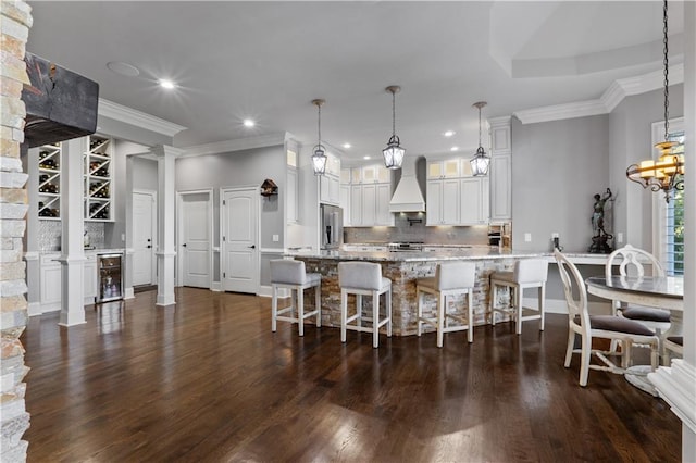 kitchen with stainless steel appliances, decorative columns, a kitchen breakfast bar, premium range hood, and dark wood-type flooring