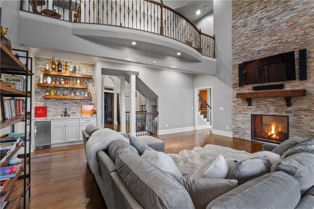 living room featuring decorative columns, dark hardwood / wood-style floors, a towering ceiling, a stone fireplace, and indoor bar