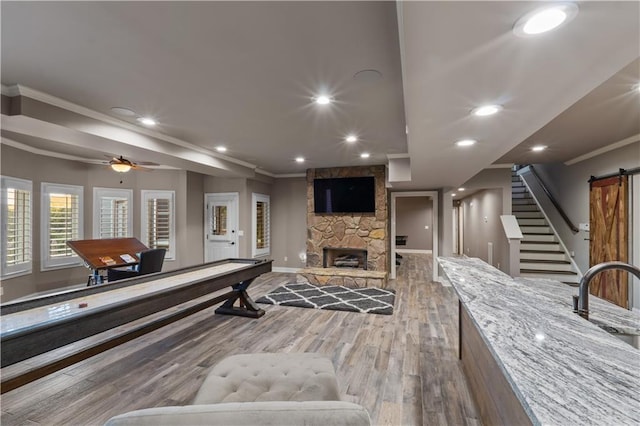 recreation room featuring a fireplace, hardwood / wood-style floors, ornamental molding, ceiling fan, and a barn door