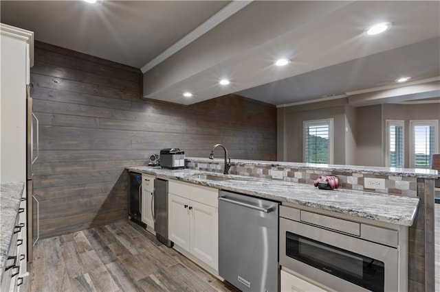 kitchen with white cabinets, appliances with stainless steel finishes, dark hardwood / wood-style flooring, sink, and wood walls