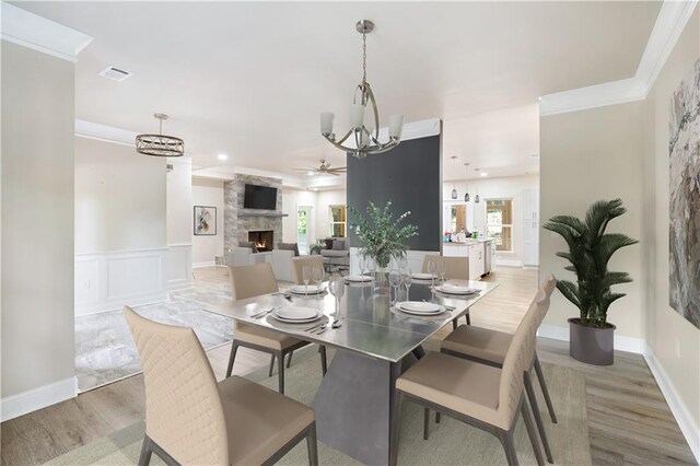 dining room featuring crown molding, a fireplace, ceiling fan with notable chandelier, and hardwood / wood-style flooring