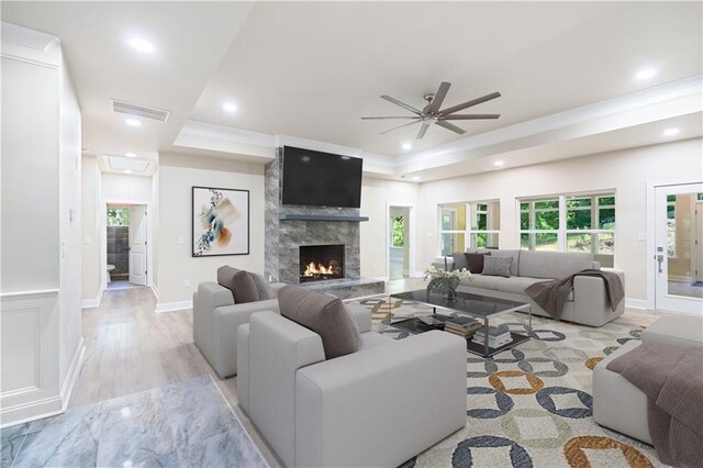 living room featuring ceiling fan, light wood-type flooring, a fireplace, and a tray ceiling