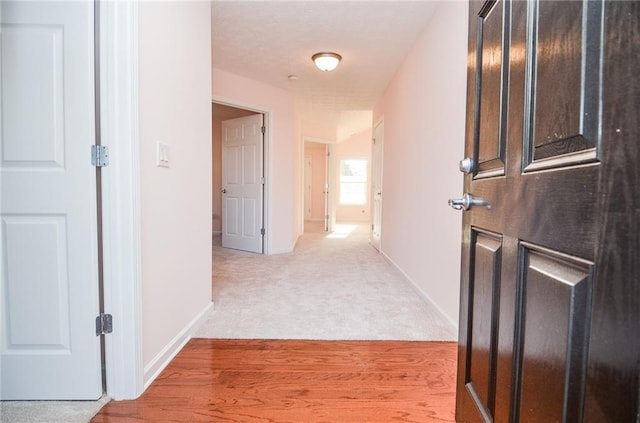 corridor featuring light wood finished floors, light colored carpet, and baseboards