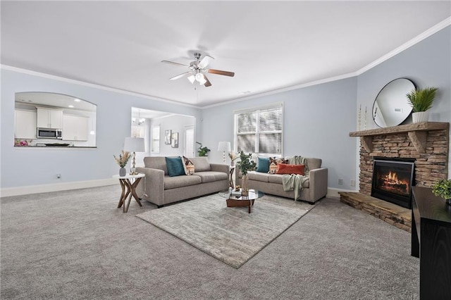 living room featuring carpet floors, crown molding, a stone fireplace, and baseboards