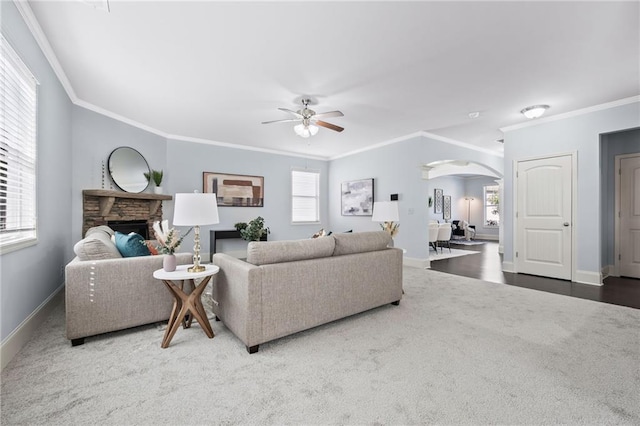 carpeted living area with arched walkways, plenty of natural light, a fireplace, and baseboards