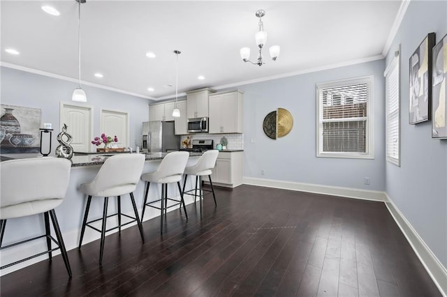 kitchen with dark wood-style floors, appliances with stainless steel finishes, a breakfast bar, and baseboards