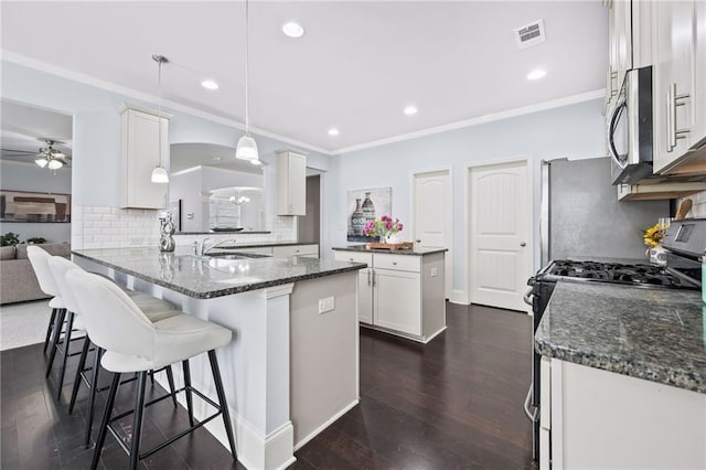 kitchen with stainless steel appliances, visible vents, dark wood-type flooring, white cabinets, and a peninsula