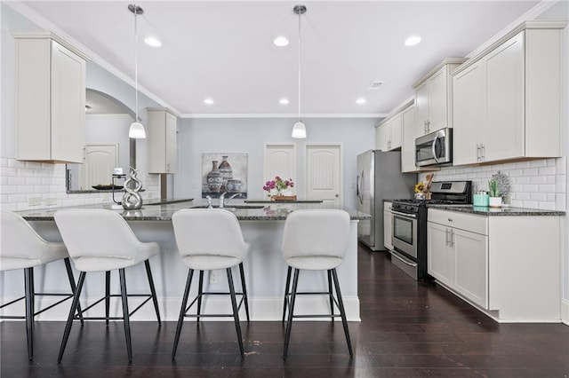 kitchen with a peninsula, dark wood-style flooring, a kitchen breakfast bar, appliances with stainless steel finishes, and dark stone countertops