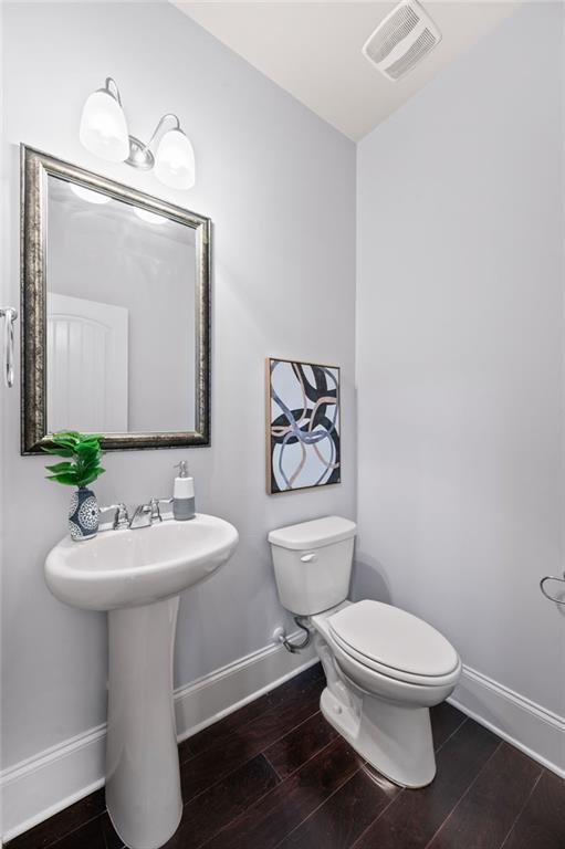 bathroom with toilet, wood finished floors, visible vents, and baseboards