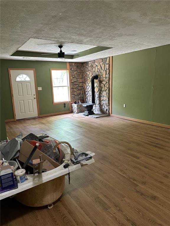 unfurnished living room with a wood stove, wood finished floors, a textured ceiling, baseboards, and a ceiling fan