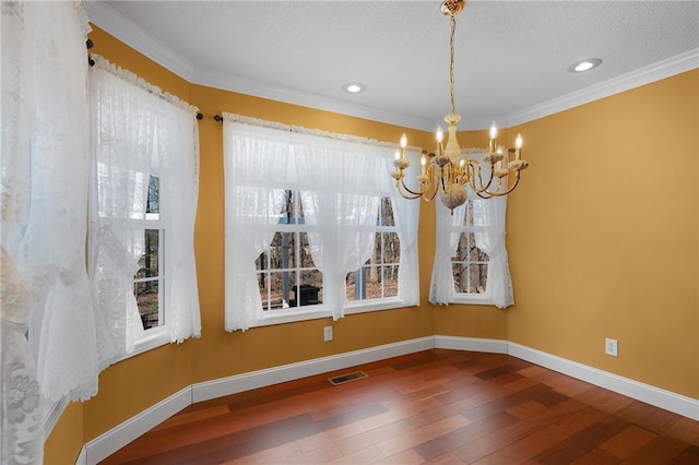 unfurnished dining area featuring hardwood / wood-style floors, baseboards, visible vents, ornamental molding, and a chandelier