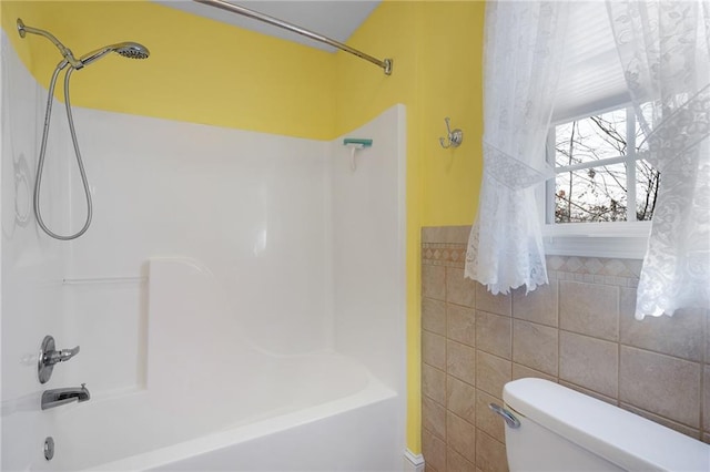 bathroom with toilet, tile walls, and  shower combination