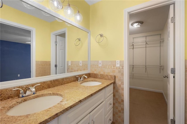 bathroom featuring tile walls, a spacious closet, double vanity, and a sink