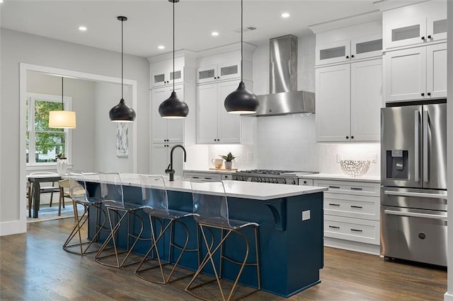 kitchen featuring wall chimney range hood, a breakfast bar area, a kitchen island with sink, white cabinetry, and stainless steel appliances