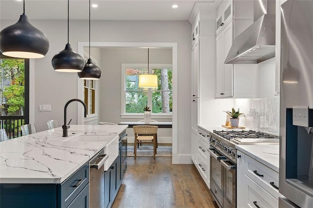 kitchen featuring wall chimney exhaust hood, white cabinetry, stainless steel appliances, and hanging light fixtures