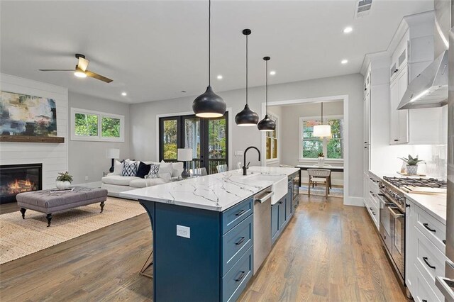 660 Timm Valley Rd NE, Atlanta, GA 30305 - kitchen featuring blue cabinetry, stainless steel appliances, white cabinetry, a breakfast bar area, and wall chimney range hood
