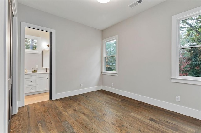 unfurnished bedroom featuring ensuite bath and dark hardwood / wood-style flooring