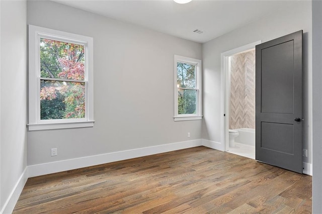 unfurnished bedroom with ensuite bath and hardwood / wood-style floors