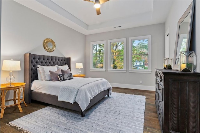 bedroom with a raised ceiling, dark wood-type flooring, and ceiling fan