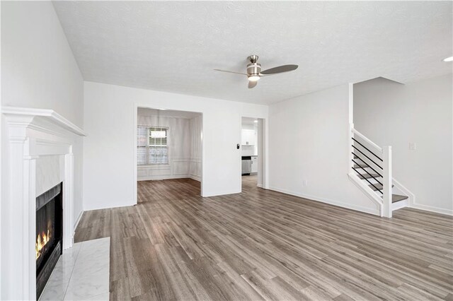 unfurnished living room featuring ceiling fan, a textured ceiling, a fireplace, and wood-type flooring