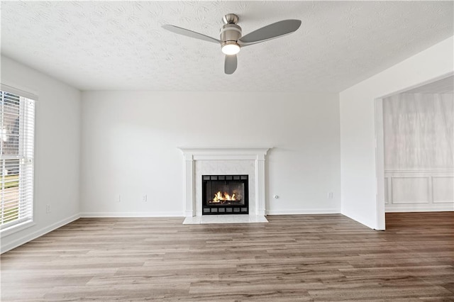 unfurnished living room featuring ceiling fan, a tile fireplace, hardwood / wood-style floors, and a textured ceiling