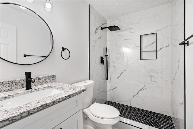 bathroom with a tile shower, vanity, and toilet