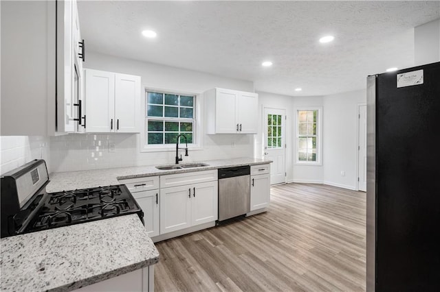 kitchen with white cabinets, light stone countertops, sink, appliances with stainless steel finishes, and light wood-type flooring