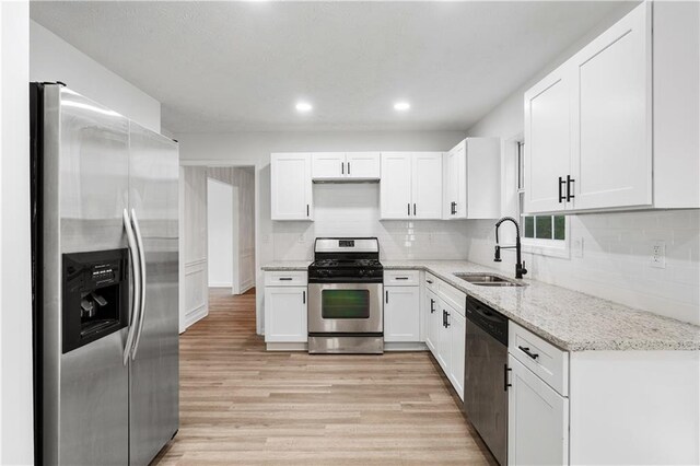 kitchen featuring sink, white cabinetry, light hardwood / wood-style flooring, appliances with stainless steel finishes, and light stone countertops