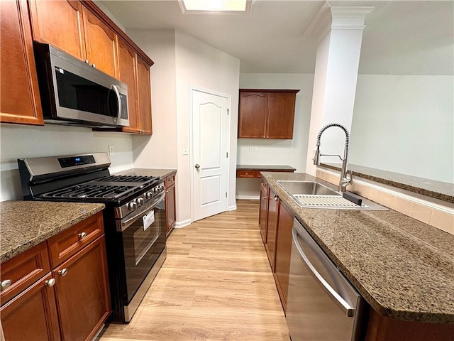 kitchen featuring appliances with stainless steel finishes, dark stone counters, light wood-style floors, and a sink