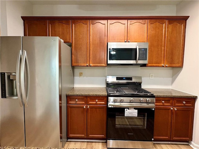 kitchen with dark stone countertops, stainless steel appliances, and light wood-style floors