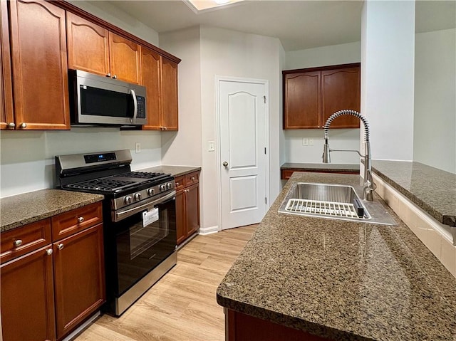 kitchen featuring dark stone countertops, stainless steel appliances, light wood finished floors, and a sink