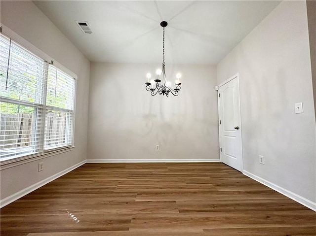 unfurnished dining area featuring a chandelier, visible vents, wood finished floors, and baseboards