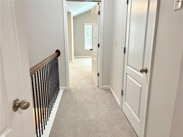corridor with an upstairs landing, baseboards, lofted ceiling, and light carpet