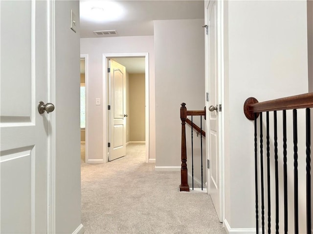 hallway with an upstairs landing, visible vents, carpet floors, and baseboards