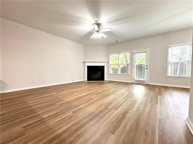 unfurnished living room featuring ceiling fan, baseboards, wood finished floors, and a fireplace