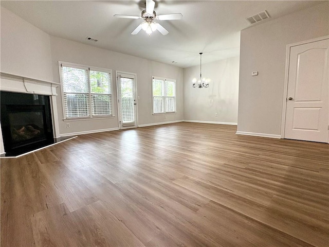 unfurnished living room with visible vents, baseboards, a fireplace, wood finished floors, and ceiling fan with notable chandelier