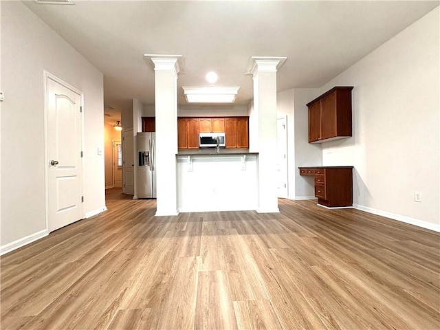 unfurnished living room with ornate columns, light wood-style floors, and baseboards