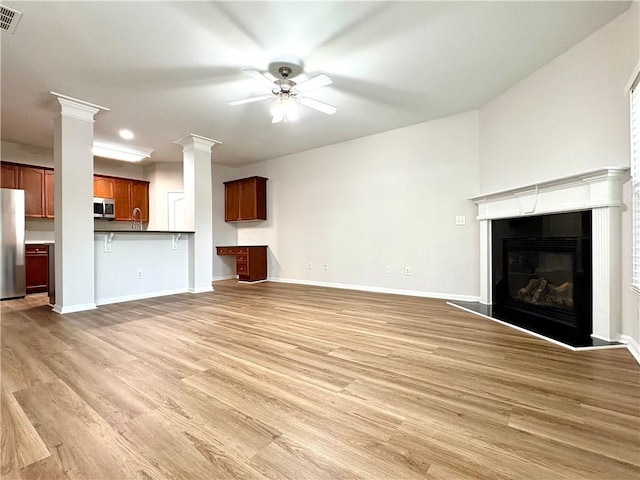 unfurnished living room with light wood-style flooring, visible vents, baseboards, a glass covered fireplace, and a ceiling fan