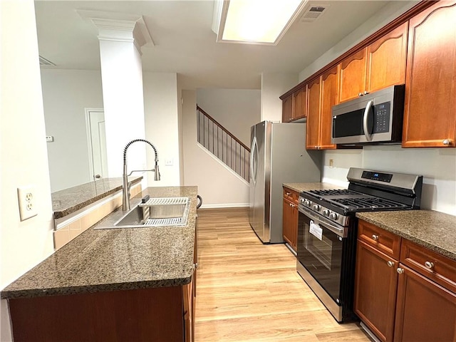 kitchen featuring dark stone counters, light wood-style floors, appliances with stainless steel finishes, a sink, and visible vents