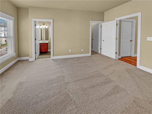 unfurnished bedroom with light colored carpet, ensuite bathroom, and baseboards