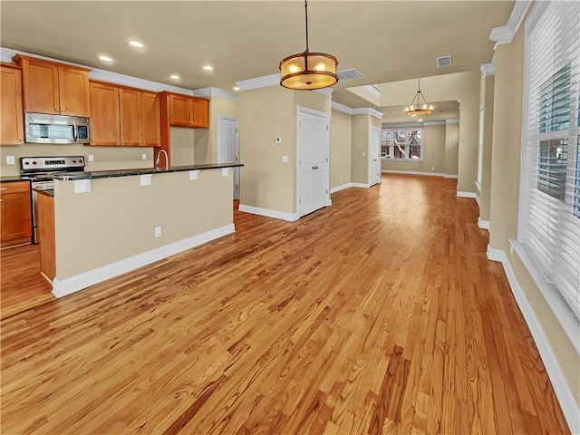 kitchen with an island with sink, dark countertops, open floor plan, appliances with stainless steel finishes, and light wood finished floors