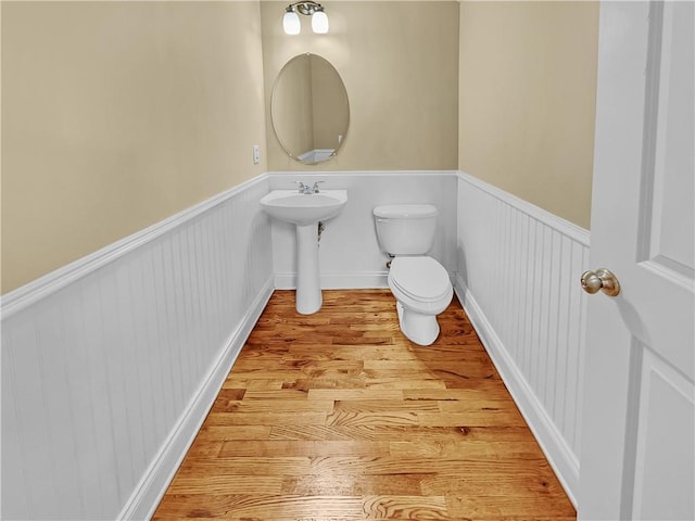 half bathroom with toilet, wood finished floors, and a wainscoted wall