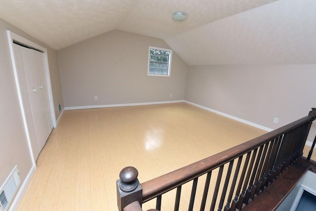 bonus room with a textured ceiling, wood-type flooring, and lofted ceiling