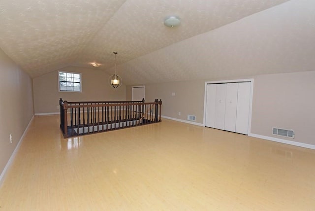 bonus room with a textured ceiling, wood-type flooring, and vaulted ceiling