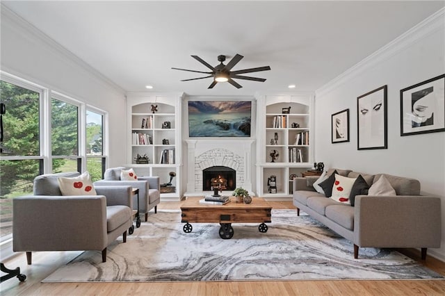 4030 Scenic View Ct, Cumming, GA 30028 - living room featuring a warm lit fireplace, built in shelves, ceiling fan, crown molding, and wood finished floors