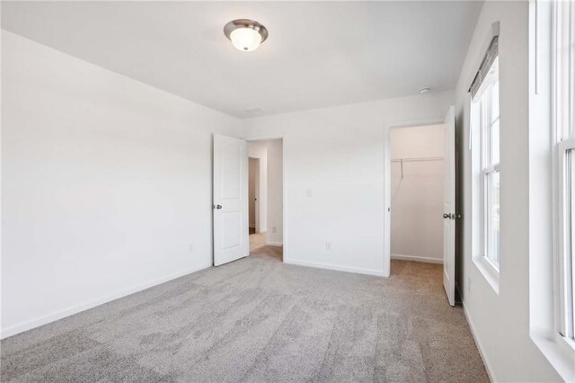 unfurnished bedroom featuring a spacious closet, a closet, and light colored carpet